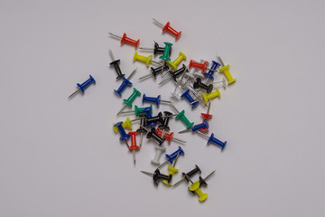 Thumbtacks of different bright colors are scattered randomly on a gray background.