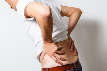 Lumbago symptom. Young man holding his painful inflamed loin. Health care and medicine.