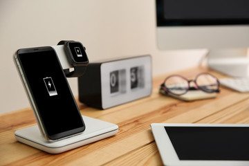 Mobile phone and smartwatch with wireless charger on wooden table. Modern workplace accessory