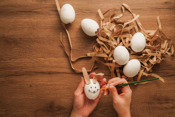 painting an egg in hand like a rabbit face and other white egg on wooden table