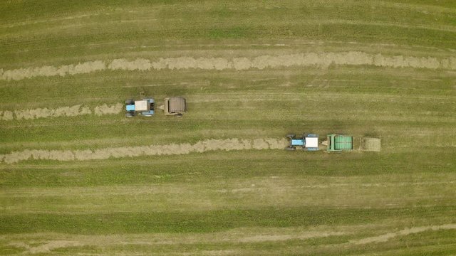 Aerial view of two tractors collecting crop straw and making haystacks in baler.