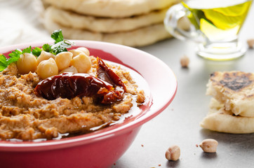 Closeup view at hummus topped with sun dried tomatoes and green coriander leaves on stone table served with traditional pita bread