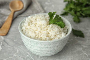 Bowl with tasty cooked rice and parsley on light grey marble table, closeup