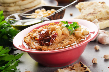 Low angle view at Hummus topped with chickpeas, olive oil green coriander leaves and sun dried tomatoes on stone table with pita bread aside