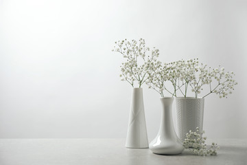 Gypsophila flowers in vases on table against white background. Space for text