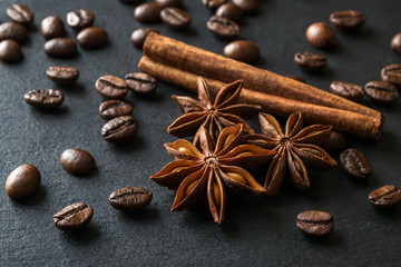 Fototapeta na wymiar Star anise, cinnamon stick and roasted coffee beans scattered on a black textured stone surface. Low key image of coffee drink ingredients.