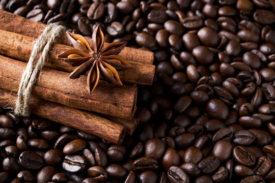 Cinnamon sticks and star anise on a roasted coffee beans background. Low key image of coffee drink ingredients.