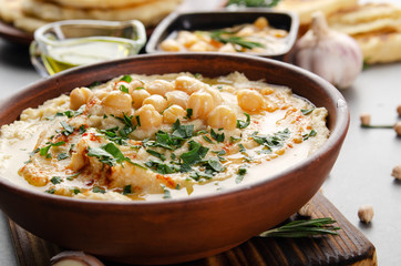 Fresh homemade Hummus in clay dish topped with olive oil, chickpeas and chopped green coriander leaves on stone table served with spices