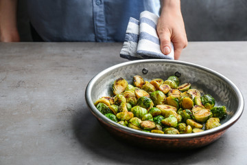 Woman holding pan with roasted Brussels sprouts at light table, closeup