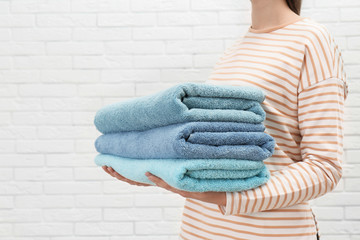 Woman holding fresh towels against white brick wall, closeup