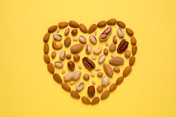 Heart made of different nuts on yellow background, flat lay