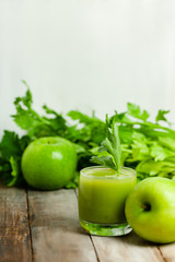 Healthy food, vegan diet concept - glass of fresh green juice or smoothie with celery, apple, orange. Antioxidant fresh detox beverage with raw ingredients.  Close up, wooden background, copy space