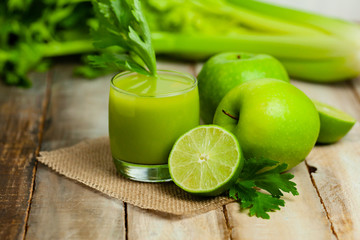 Healthy food, vegan diet concept - glass of fresh green juice or smoothie with celery, apple, orange. Antioxidant fresh detox beverage with raw ingredients.  Close up, wooden background