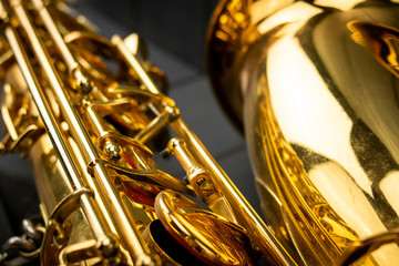Fototapeta na wymiar Keys, rods and bell of a golden and shiny saxophone, in the foreground, on gray wooden background