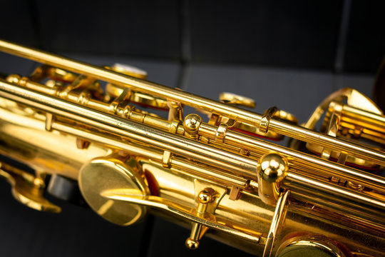 Keys and rods of a golden and shiny saxophone, in the foreground, on gray wooden background