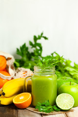 Healthy food and vegan diet concept - mason jar of fresh green juice or smoothie with celery, orange, banana, apple. Antioxidant detox beverage with raw ingredients.  Wooden background, copy space