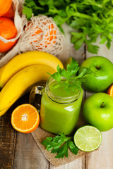 Healthy food and vegan diet concept - mason jar of fresh green juice or smoothie with celery, orange, banana, apple. Antioxidant detox beverage with raw ingredients.  Wooden background.