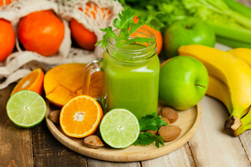 Healthy food and vegan diet concept - mason jar of fresh green juice or smoothie with celery, orange, banana, apple. Antioxidant detox beverage with raw ingredients.  Wooden background.