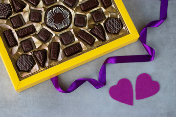 Box of chocolates, two purple decorative hearts and purple ribbon on gray background. Valentines day concept.