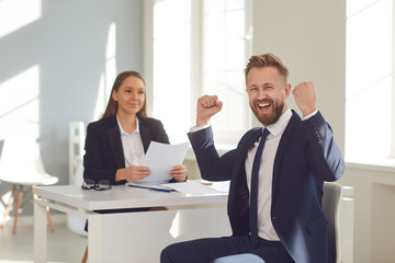 Successful interview. A man in a suit rejoices at a new job sitting at a table with a woman employer in a white office.