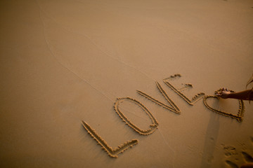 Girl's hand with an engagement ring in a heart drawn on the sand. Written in the sand the word Love