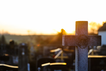 Cruz de un cementerio de piedra con el reflejo del sol por detrás al atardecer. 
