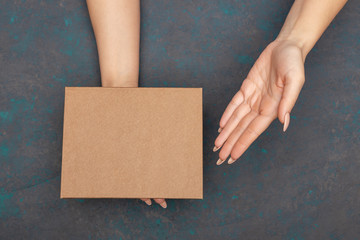 Female hands holding and showing on cardboard box with empty copy space topsheet over dark wooden background.