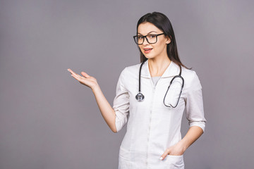 Portrait of cheerful young female doctor with stethoscope over neck looking at camera isolated on grey background.