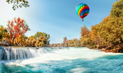 A beautiful multi-colored balloon flies over an autumn waterfall on the Manavgat River in Antalya, Turkey. Panoramic view.