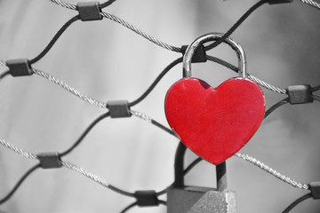 Padlock in the red heart shape on the fence of a bridge. Symbol of love forever. Monochrome background.