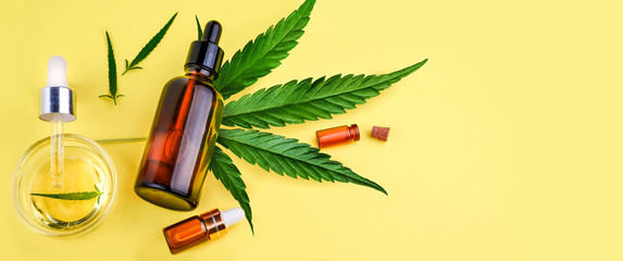 Glass bottles with CBD oil, THC tincture and hemp leaves on a yellow background. Flat lay,...