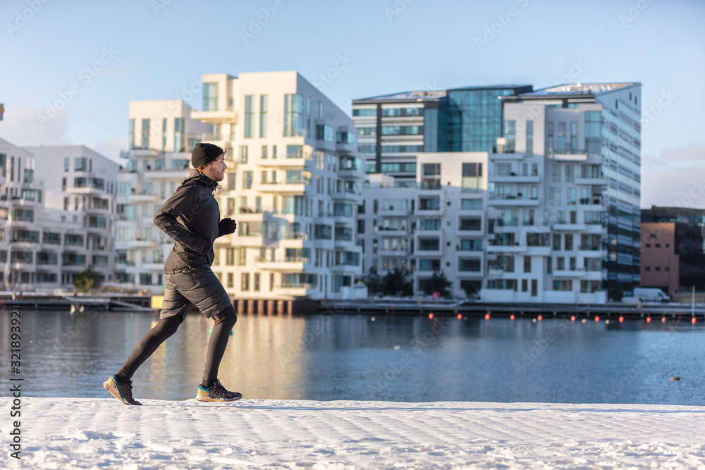 Wall mural Winter run city lifestyle runner athlete man jogging outside on modern urban harbour street waterfront. Running active living healthy people.