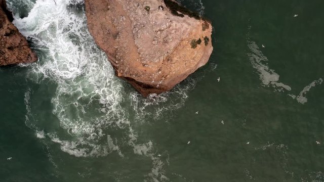 Rising drone shot over the La Roche Percee, a prominent geologic feature 200m from the the coast and surfing beaches of Biarritz, France.