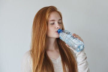 portrait of pretty healthy beautiful young girl drinking water from blue plastic bottle