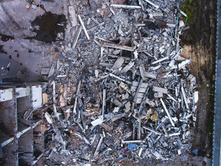 A process of buliding demolition, demolition site with heavy bulldozer and excavator with crushing equipment at work, demolished house, shot from air with drone