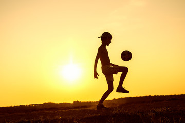 Fototapeta premium Boy playing with ball in nature in hot evening, silhouette of playing child at sunset in countryside