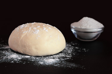 Yeast dough and bowl with flour on a dark background