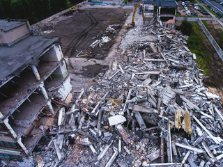 A process of buliding demolition, demolition site with heavy bulldozer and excavator with crushing equipment at work, demolished house, shot from air with drone