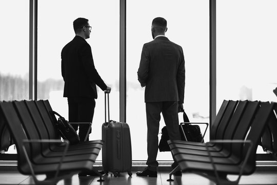 Silhouette of two businessman standing in front of a big window at airport at wating area near departure gate