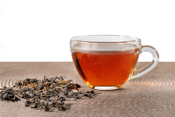 Glass cup of tea and dry leaves on a white background.