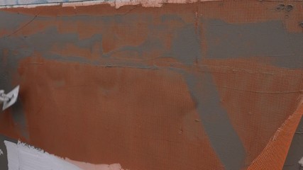 A worker working on a wall insulation, he is putting an orange fiberglass mesh over the mortar on a wall...
