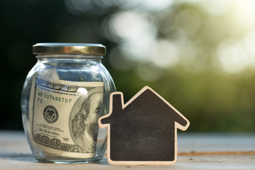 Real estate concept - money jar and little house with space for text on the wooden table in the...