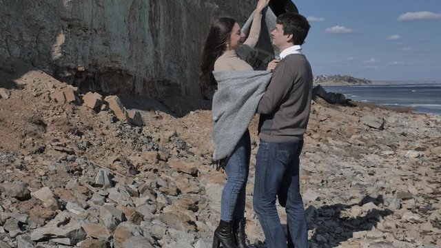 Young couple walk on a rocky shore near a rock near a river covered with ice, sunny spring day