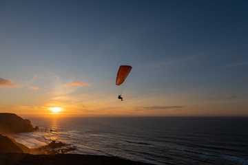 Paraglider flying over thesea shore at sunset. Paragliding sport concept.