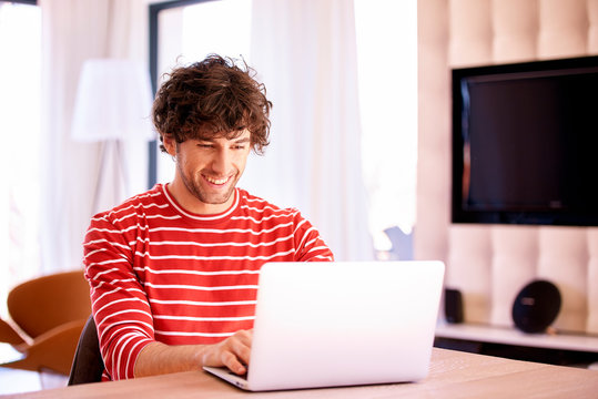 Casual man with toothy smile using his laptop at home