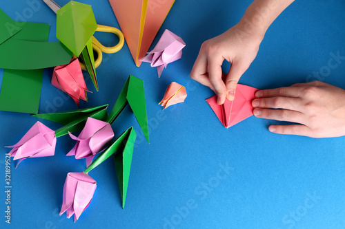 Mother's day gift. Hands of a child. Mother's Day, happy birthday, March 8, Women's Day, Valentine's Day. Bouquet of tulips from origami colored paper on a blue background. copy space.
