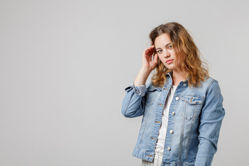 Young girl with long flowing hair in a denim looks thoughtfully at the camera and touches her hair....