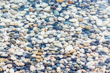 Sea coast covered with colorful pebbles. Soft transparent wave, marine background.