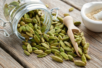 Green aromatic cardamom pods. Jar of whole cardamom pods and mortar of crushed seeds on table. - obrazy, fototapety, plakaty
