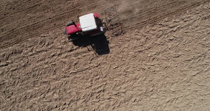 Aerial footage from a birds view of a tracktor with a spike tooth harrow cutting through clods, manure, and grasses to break up material into finer pieces so that it can be spread evenly across the gr